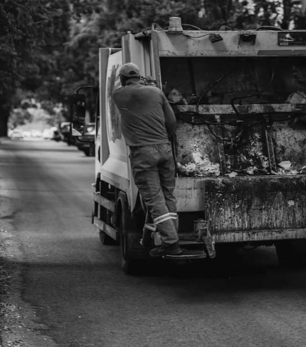 Sanitation worker riding on the back of a garbage truck collecting waste on a residential street