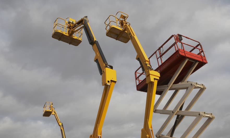Three boom lifts and a scissor lift fully extended into a cloudy sky.